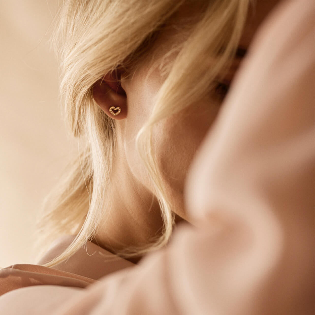 A model wearing the 8mm Brilliance Heart Hollow Earrings in golden titanium