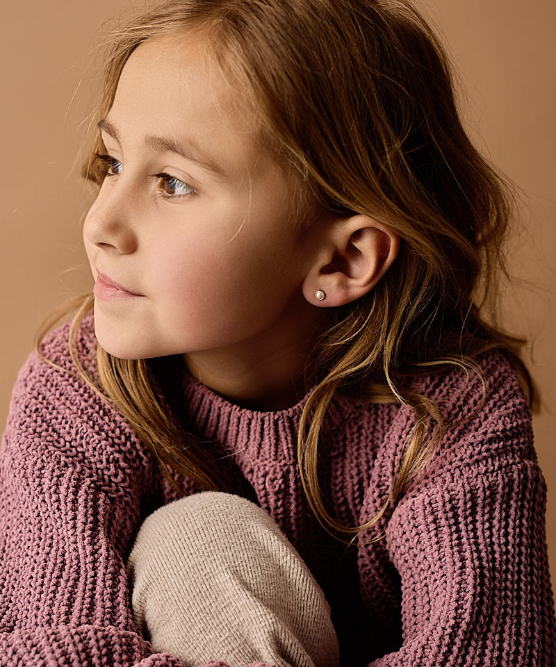 Young person wearing the golden titanium 5mm Swarovski pearl earrings in a light rose color