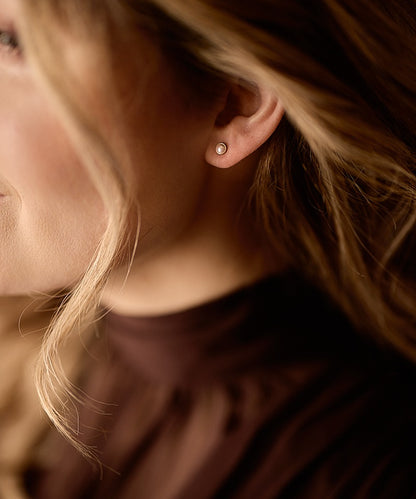 Close up of a person wearing the nickel-free golden titanium 5mm Swarovski pearl earrings in a light rose color