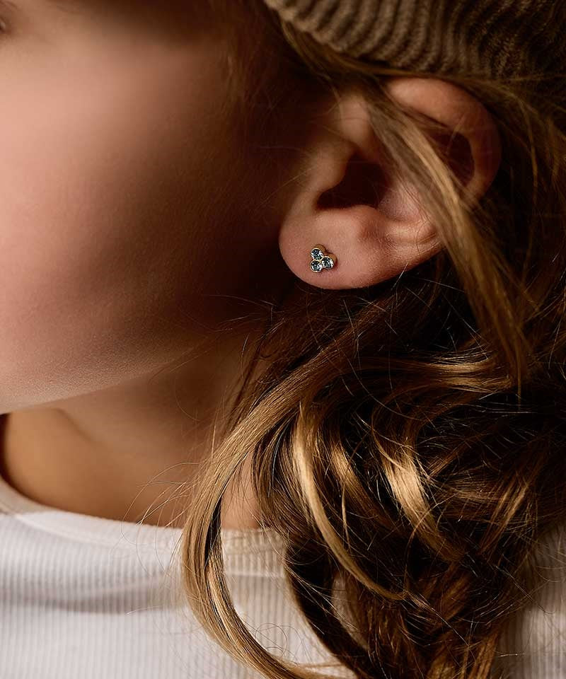 Close up of a person wearing the nickel-free Golden Titanium 6mm clover earrings with aquamarine colored Swarovski crystal stones.
