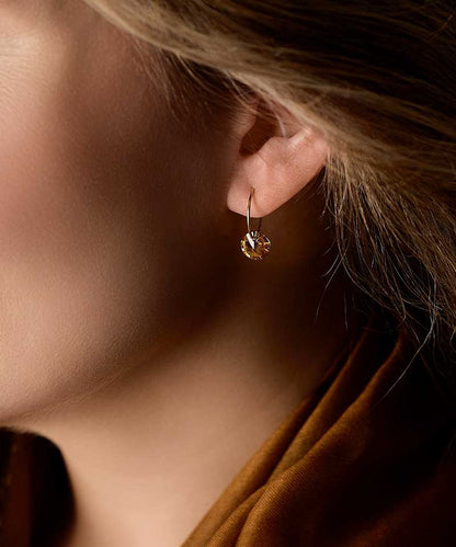 Close up of a person wearing the hypoallergenic golden titanium 14mm pendants with a round bronze colored Swarovski crystal stone
