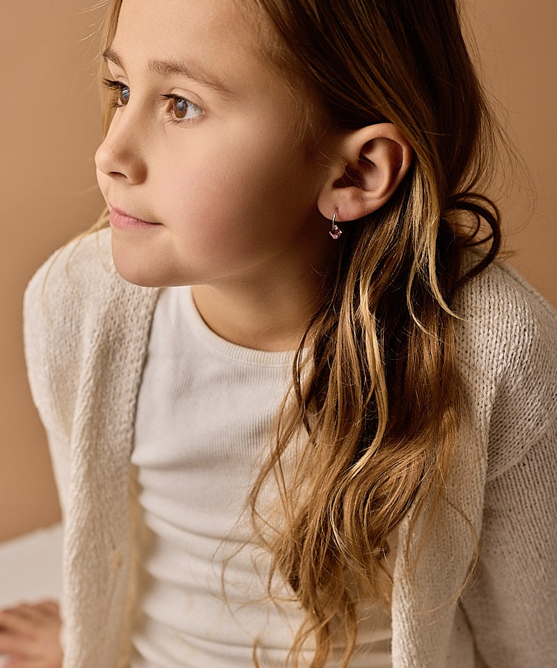 Close-up of a young girl wearing the golden titanium 12mm light rose pendant earrings, with a neutral background