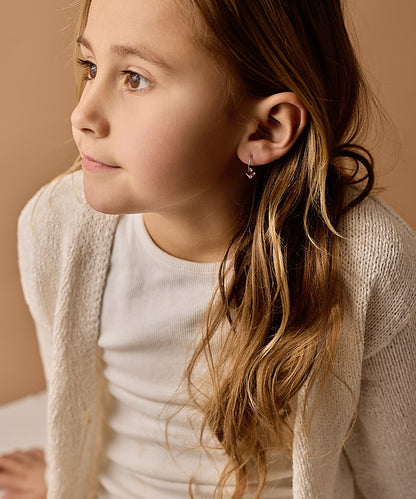 Close-up of a young girl wearing the golden titanium 12mm light rose pendant earrings, with a neutral background
