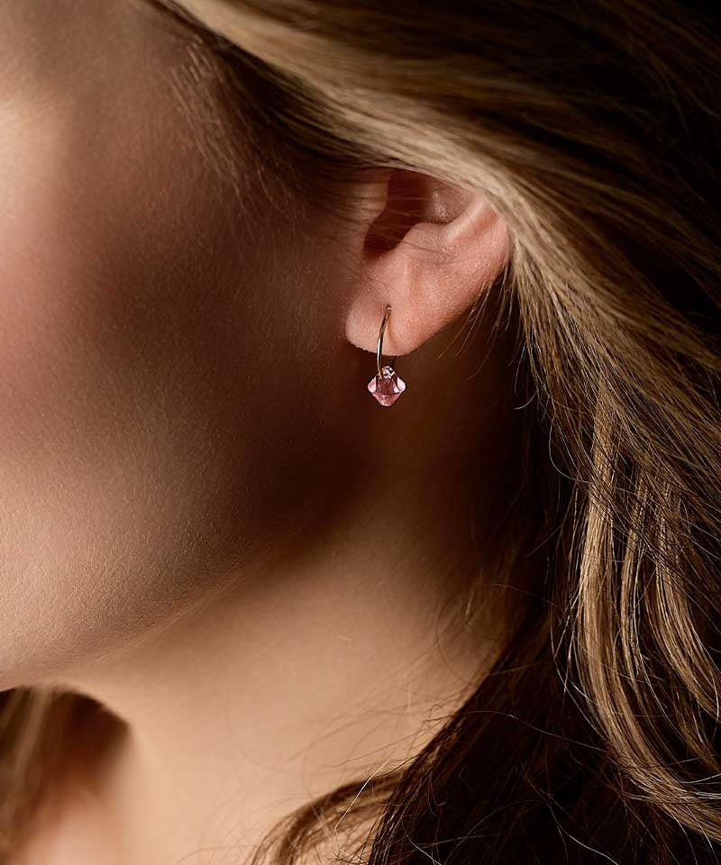 A close up image of the hypoallergenic golden titanium 12mm pendant earrings with a sparkling light rose crystal.