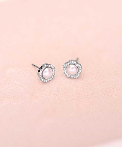 A pair of silver stud earrings with oval pink pearls surrounded by a halo of small clear crystals, displayed on a soft pink textured surface.