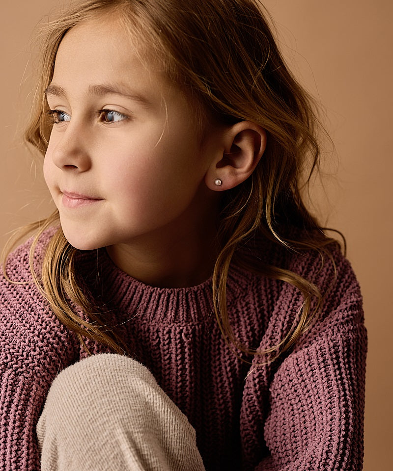 Young girl wearing a purple sweater against a beige background wearing the  5mm Silver Titanium Bezel Light Rose Swarovski Pearl earrings