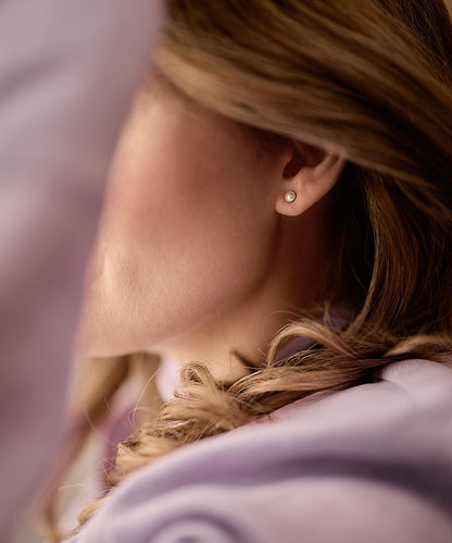Close-up of a person wearing the 5mm Silver Titanium Bezel Light Rose Swarovski Pearl earrings